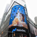 Curved blue SpaceX billboard on a Nasdaq building in Times Square showing a rocket launch and the Nasdaq sign below.