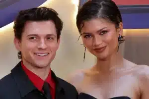 Two people posing together at an event, smiling for the camera; man in a black suit with a red shirt, woman in a black dress with long earrings.