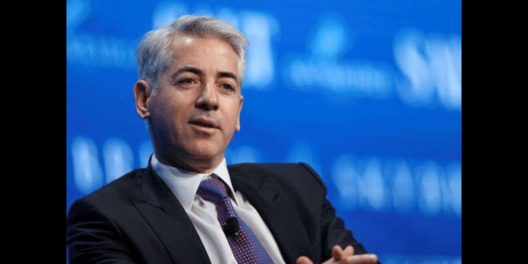 Man in a dark suit and purple tie speaking at a conference on a blue backdrop.