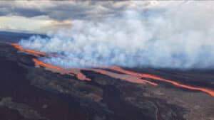 Volcanic lava stream flows across dark terrain with thick white smoke rising above it.