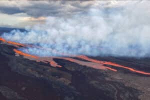 Volcanic lava stream flows across dark terrain with thick white smoke rising above it.