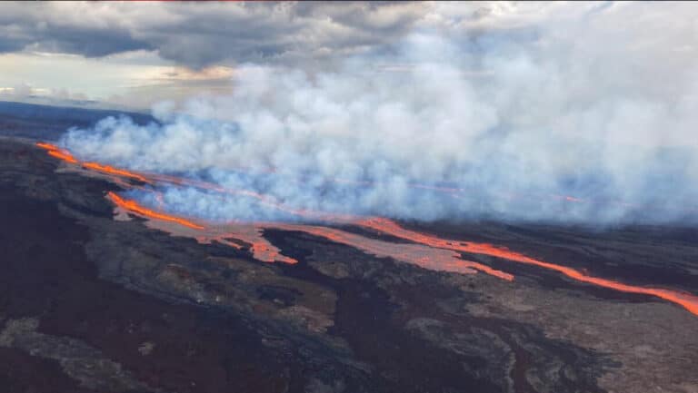 Volcanic lava stream flows across dark terrain with thick white smoke rising above it.