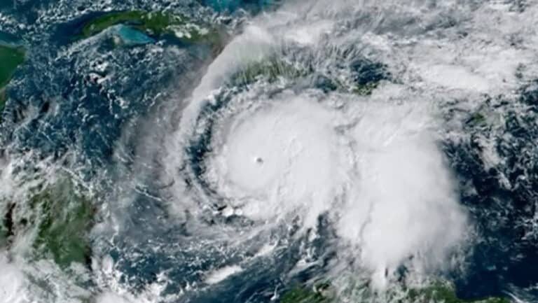 Satellite image of a large hurricane with a clear eye, spiraling white clouds over the Atlantic Ocean seen from space, near landmasses