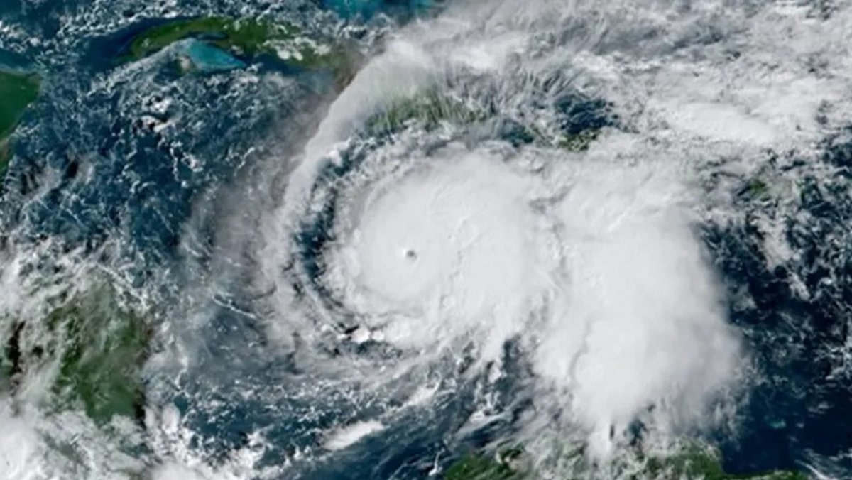 Satellite image of a large hurricane with a clear eye, spiraling white clouds over the Atlantic Ocean seen from space, near landmasses