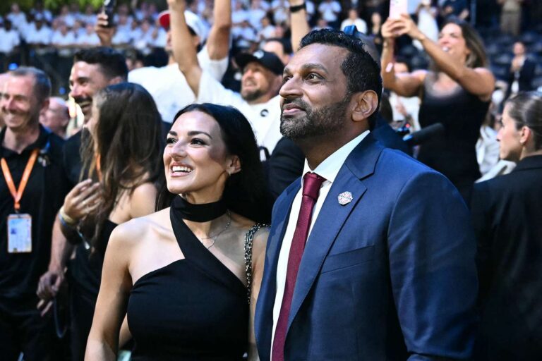 Couple in formal attire at a crowded event, smiling as fans and photographers surround them on the red carpet.