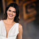 Smiling woman in a white plunging evening gown at a formal event on a red carpet image area