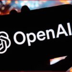 Smartphone held in hand displaying the OpenAI logo on a black screen with a colorful cityscape blur in the background, branding-focused image.