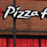 Pizza Hut storefront sign on a brick wall with a red awning, featuring the white scripted logo and the red circular emblem.