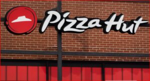 Pizza Hut storefront sign on a brick wall with a red awning, featuring the white scripted logo and the red circular emblem.
