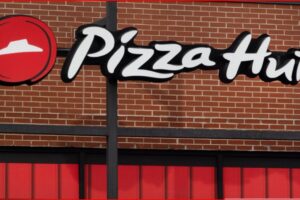 Pizza Hut storefront sign on a brick wall with a red awning, featuring the white scripted logo and the red circular emblem.
