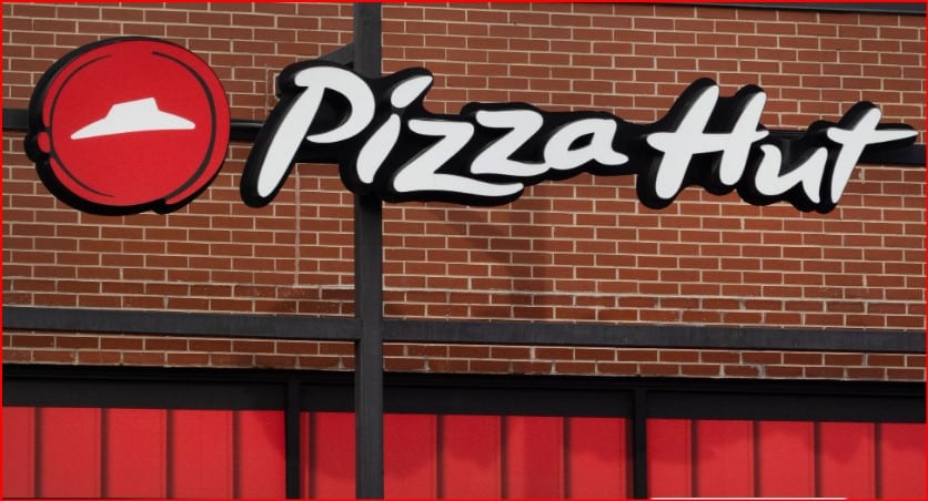 Pizza Hut storefront sign on a brick wall with a red awning, featuring the white scripted logo and the red circular emblem.