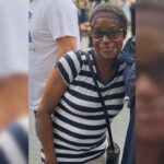 Smiling woman wearing a navy and white striped shirt, glasses, and a headband at an outdoor event.