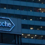 Blue, hexagonal Roche sign on office building at dusk, illuminated letters visible outside.