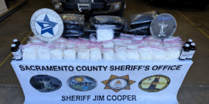 Display table of seized white powder in clear bags, with Sacramento County Sheriff's Office banner and sheriff badges in the background.