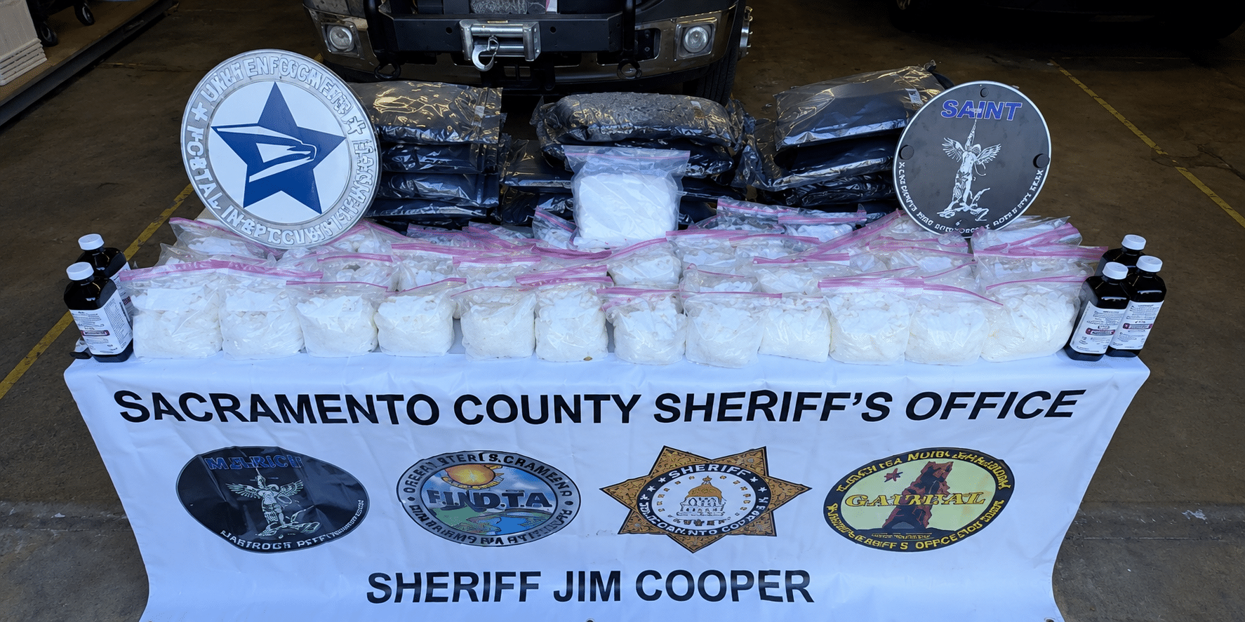 Display table of seized white powder in clear bags, with Sacramento County Sheriff's Office banner and sheriff badges in the background.