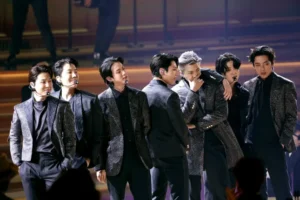 Seven male performers in glittery suits perform on a dimly lit stage reciting a choreographed routine on stage with microphones on heads set in wireless packs? (trimmed)
