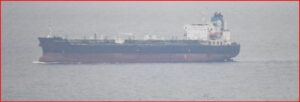 Large cargo ship on calm sea viewed from side, with a dark hull and white superstructure toward the sternsideside of the vessel.