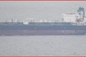 Large cargo ship on calm sea viewed from side, with a dark hull and white superstructure toward the sternsideside of the vessel.