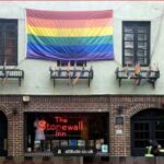 Rainbow Pride flag hangs above The Stonewall Inn on a brick building on a city street