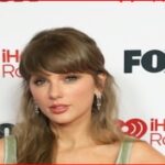 Taylor Swift posing on the red carpet at an iHeartRadio event, with FOX and iHeart logos in the background.