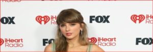 Taylor Swift posing on the red carpet at an iHeartRadio event, with FOX and iHeart logos in the background.