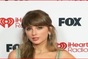 Taylor Swift posing on the red carpet at an iHeartRadio event, with FOX and iHeart logos in the background.