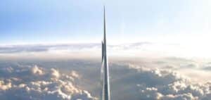 Tall, slender glass skyscraper piercing the clouds as seen from above against a blue sky.