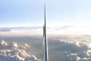 Tall, slender glass skyscraper piercing the clouds as seen from above against a blue sky.