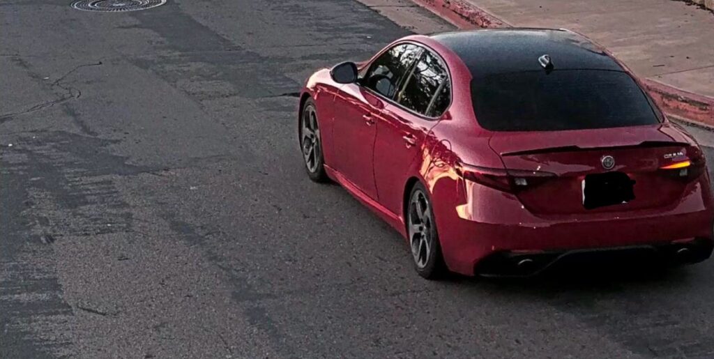 Red four-door sedan photographed from rear three-quarter view parked on a cracked urban street.