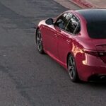 Red four-door sedan photographed from rear three-quarter view parked on a cracked urban street.
