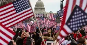 Crowd of people waving American flags in front of the U.S. Capitol dome in Washington, DC.