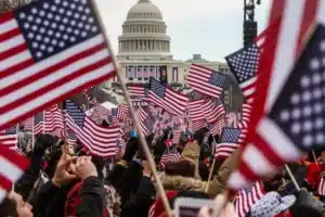 Crowd of people waving American flags in front of the U.S. Capitol dome in Washington, DC.