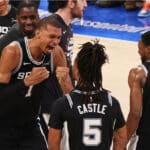 Basketball players in black jerseys celebrate on the court, fists in the air after a play.