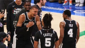 Basketball players in black jerseys celebrate on the court, fists in the air after a play.