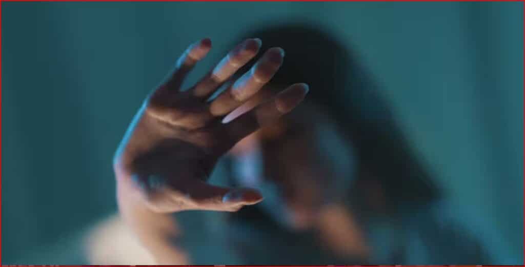 Outstretched hand reaching toward the camera in a blue-toned scene, with a blurred figure in the background.