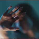 Outstretched hand reaching toward the camera in a blue-toned scene, with a blurred figure in the background.