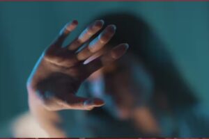 Outstretched hand reaching toward the camera in a blue-toned scene, with a blurred figure in the background.