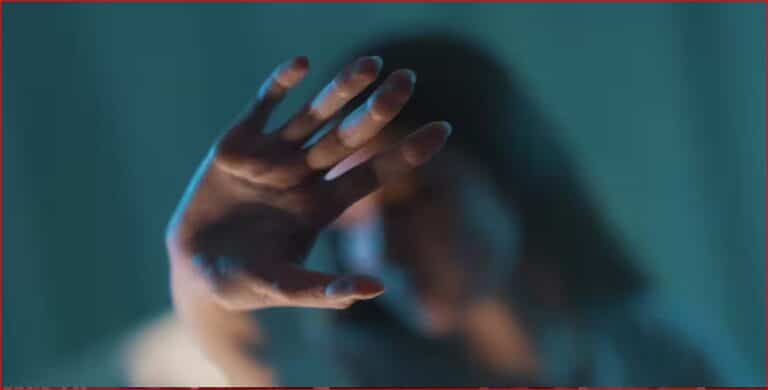 Outstretched hand reaching toward the camera in a blue-toned scene, with a blurred figure in the background.