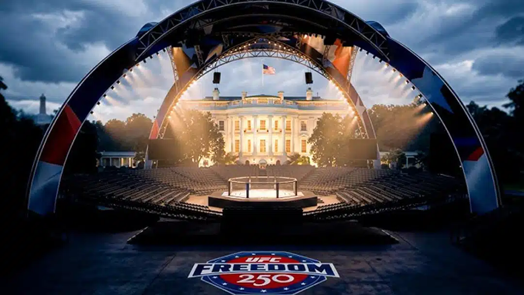 Outdoor concert stage set in front of a lit government building, with a curved truss arch, audience seating, and a UFC Freedom 250 logo on the floor in the foreground.
