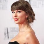 Portrait of a woman on a red carpet in a black strapless dress, with an updo and gold earrings, looking at the camera.