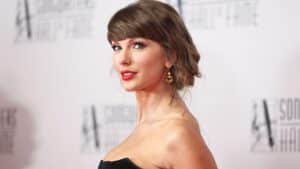 Portrait of a woman on a red carpet in a black strapless dress, with an updo and gold earrings, looking at the camera.