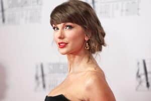 Portrait of a woman on a red carpet in a black strapless dress, with an updo and gold earrings, looking at the camera.