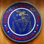 Circular seal of the Federal Communications Commission (FCC) on a wooden background, blue center with red text around the edge.