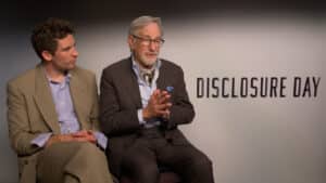 Two men in business attire sit side by side in an interview setting, with a backdrop reading DISCLOSURE DAY; the older man on the right speaks with his hands clasped.