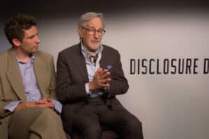 Two men in business attire sit side by side in an interview setting, with a backdrop reading DISCLOSURE DAY; the older man on the right speaks with his hands clasped.