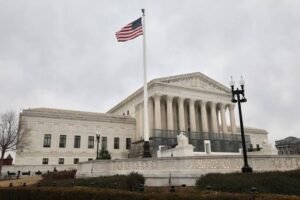 U.S. Supreme Court building with flagpole, marble steps, and neoclassical columns under a cloudy sky.