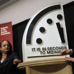 Three people beside a large Doomsday Clock reading 85 seconds to midnight at a Bulletin of the Atomic Scientists event.