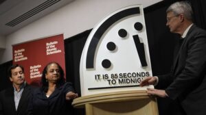Three people beside a large Doomsday Clock reading 85 seconds to midnight at a Bulletin of the Atomic Scientists event.