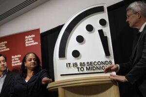 Three people beside a large Doomsday Clock reading 85 seconds to midnight at a Bulletin of the Atomic Scientists event.