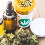 Medical marijuana bottle, cannabis oil dropper, and a jar labeled with a green leaf on a wooden surface, with cannabis buds nearby.